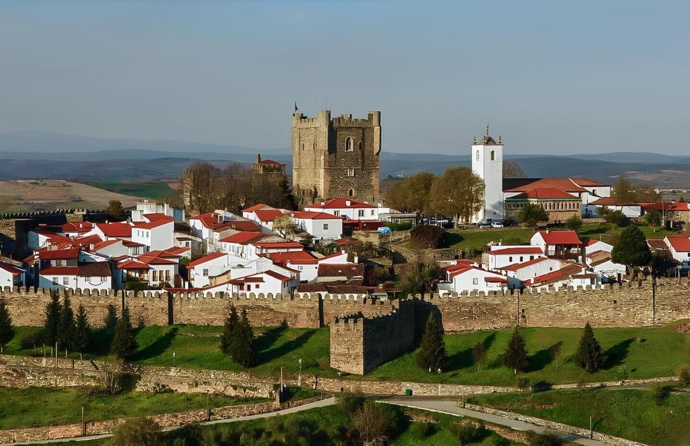 Imagem aréa da paisagem de Bragança, onde se vê o castelo, a moralha e vários edifícios, num dia com algumas núvens.