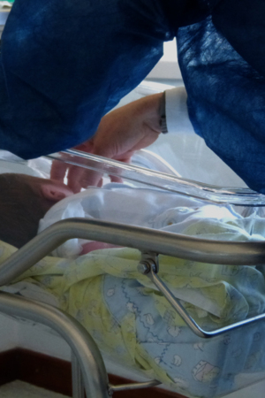 Bebé está deitado no berço do hospital enquanto um adulto o acaricia